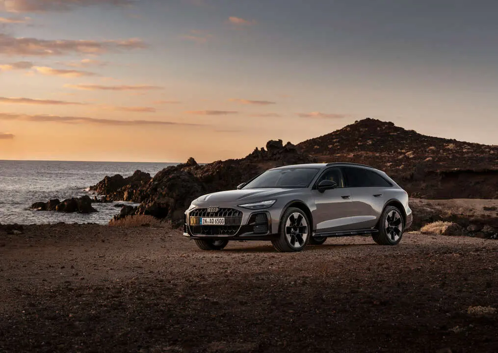 Audi A6 allroad (plateau grey metallic) in side view at a rugged coastal landscape during sunset.