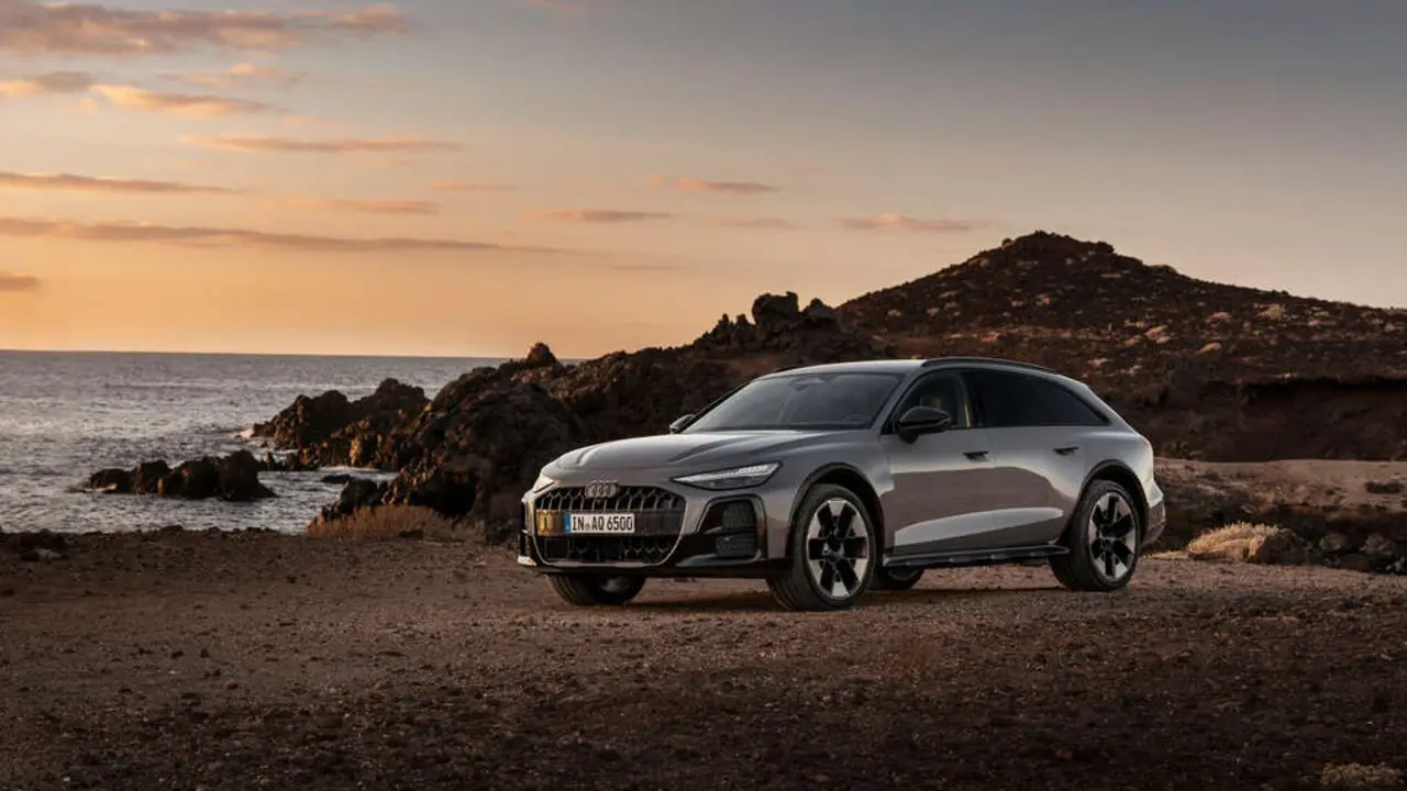 Audi A6 allroad (plateau grey metallic) in side view at a rugged coastal landscape during sunset.